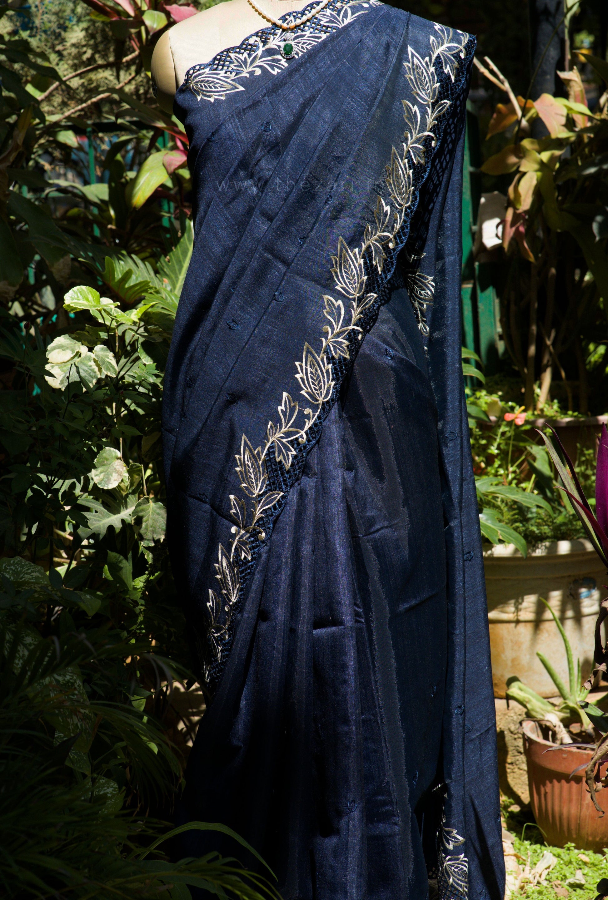 Navy blue saree with white floral patterns draped over a mannequin against a garden background.