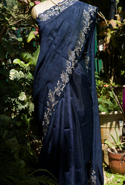 Navy blue saree with white floral patterns draped over a mannequin against a garden background.