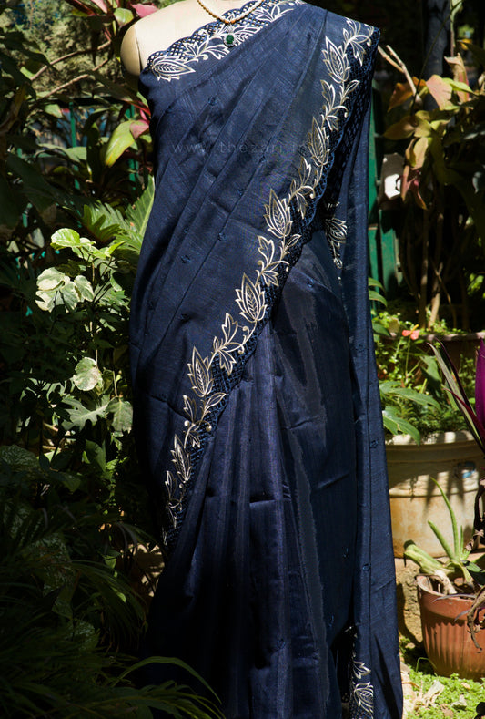 Navy blue saree with white floral patterns draped over a mannequin against a garden background.