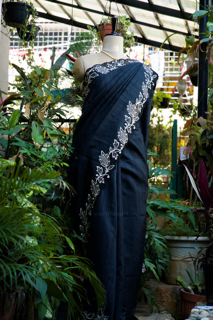 Navy blue saree with white floral patterns on a mannequin against a garden background