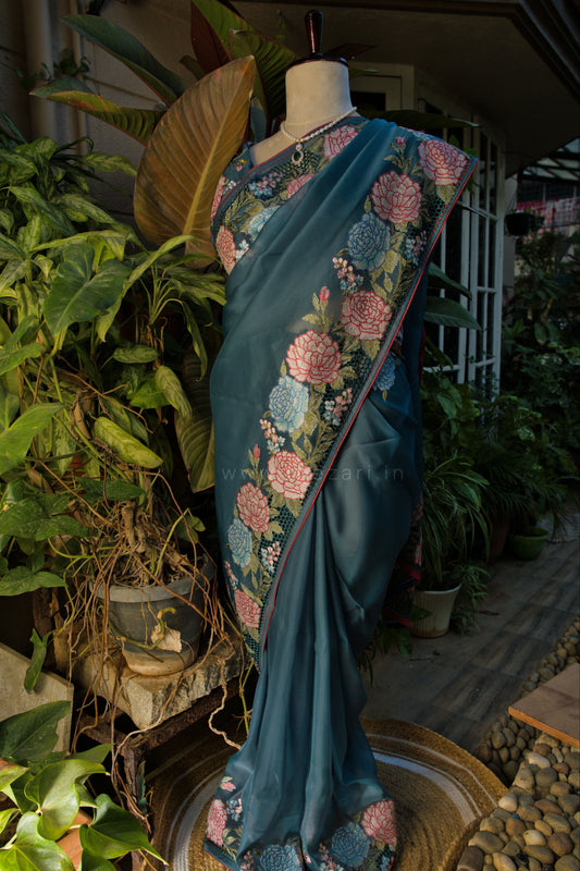 Blue saree with floral patterns on a mannequin against a natural background with plants.