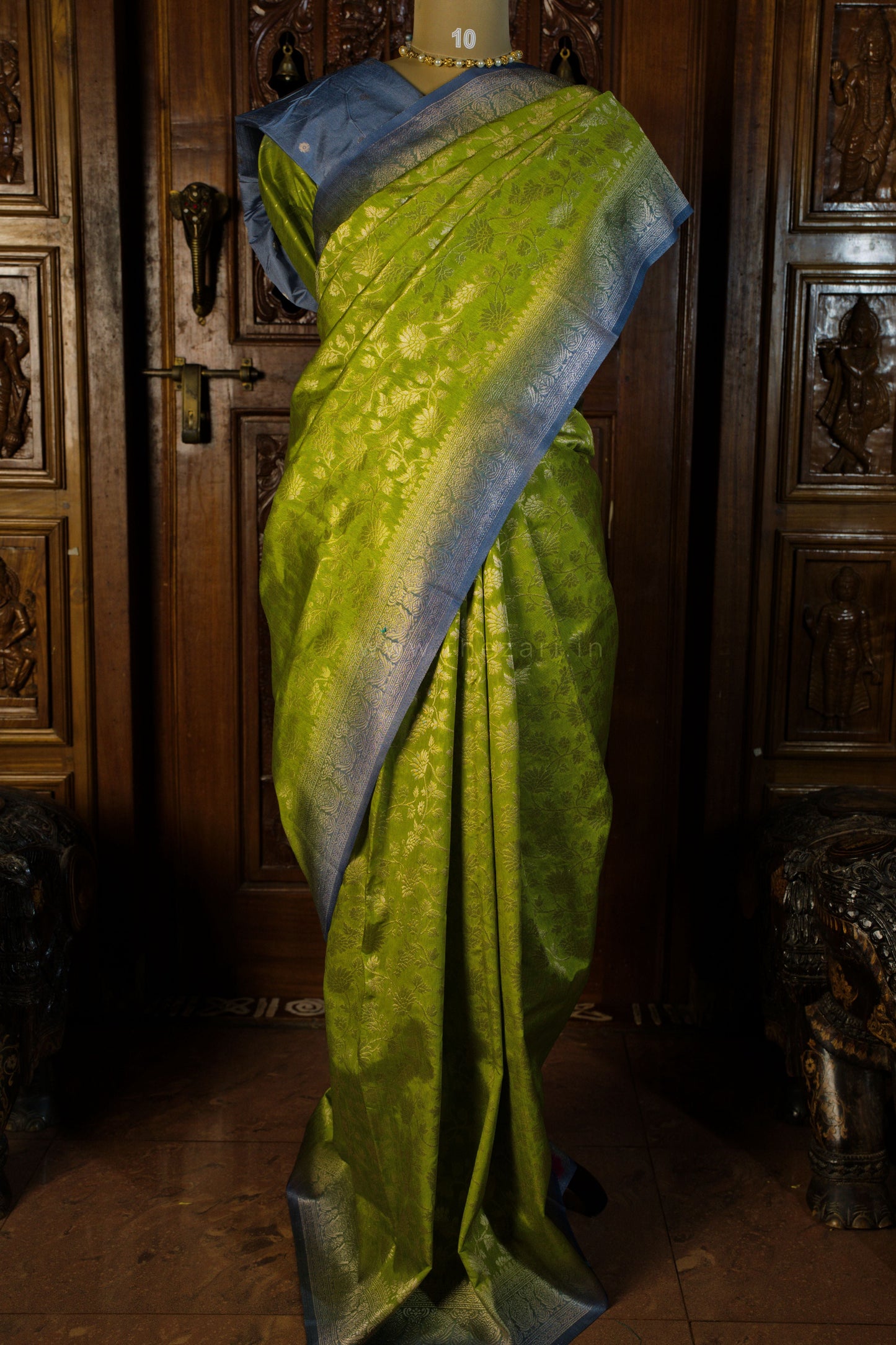 Green saree with blue border on a mannequin against a wooden background