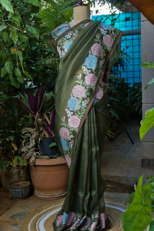 Mannequin wearing a green saree with floral patterns in an outdoor setting with plants.