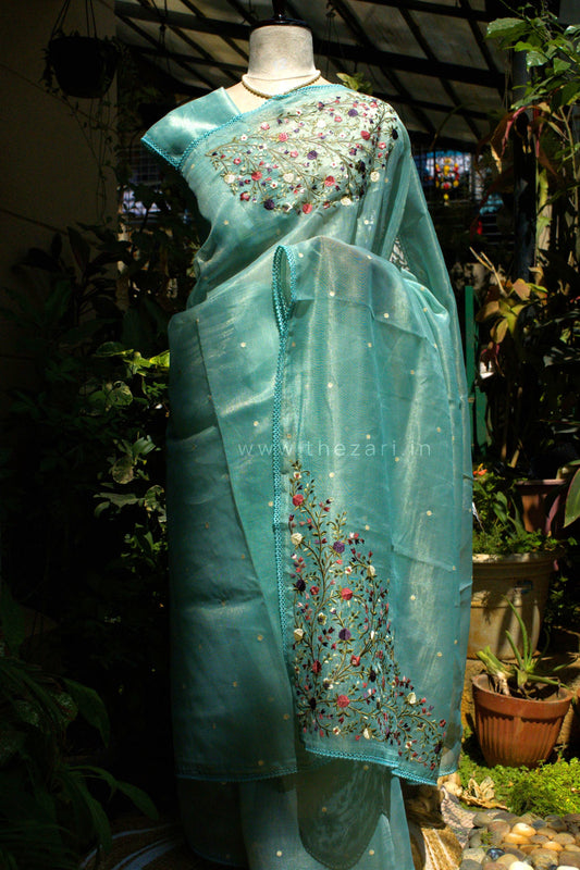 Teal saree with floral embroidery on a mannequin against a garden background