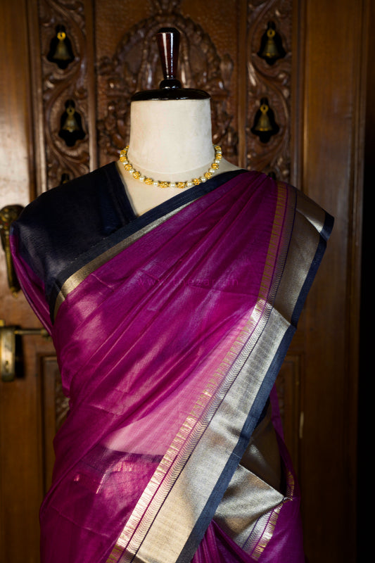 Mannequin wearing a pink saree with a black border and gold jewelry against a wooden background.