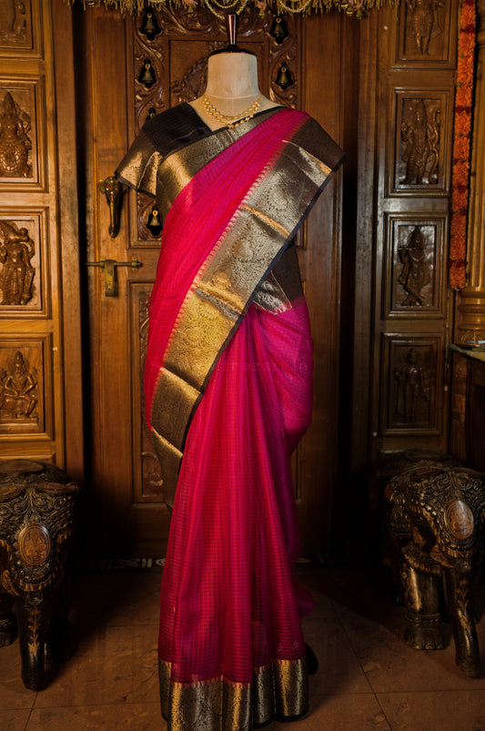 Mannequin wearing a pink saree with gold and silver border against a decorative wooden background